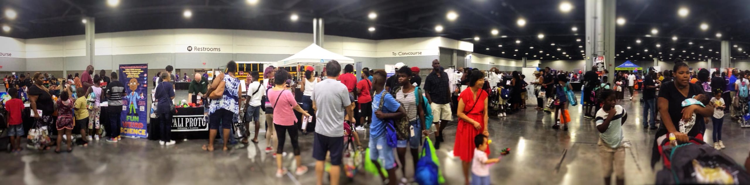 A crowd of parents, students and educators at an indoor education event. Vendor booths, including our booth are visible in the background.